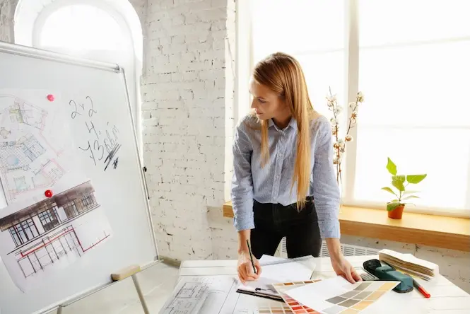 Assistante d’architecte consultant des plans et échantillons de couleurs dans un bureau d'études lumineux