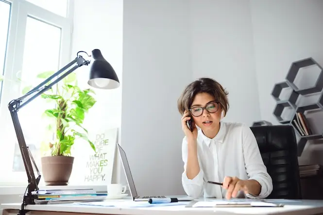 Assistante administrative en agence d'architecture au téléphone, consultant des documents à son bureau