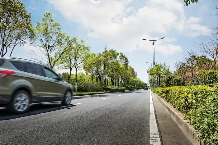 Voiture en mouvement sur une route bordée d'arbres, illustrant le calcul des frais kilométriques professionnels