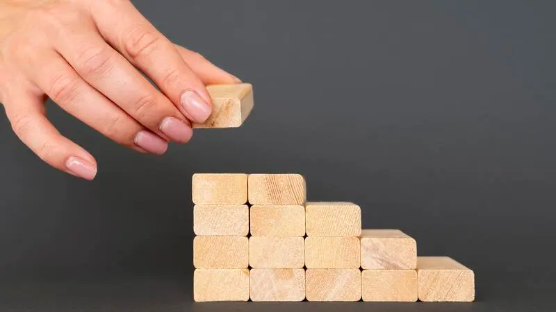 une main qui pose un dernier élément sur une construction en blocs pour symboliser une base CRM construit solidement, étape par étape